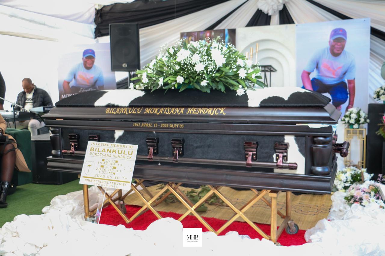 Casket with floral tribute and memorial photographs inside a draped tent