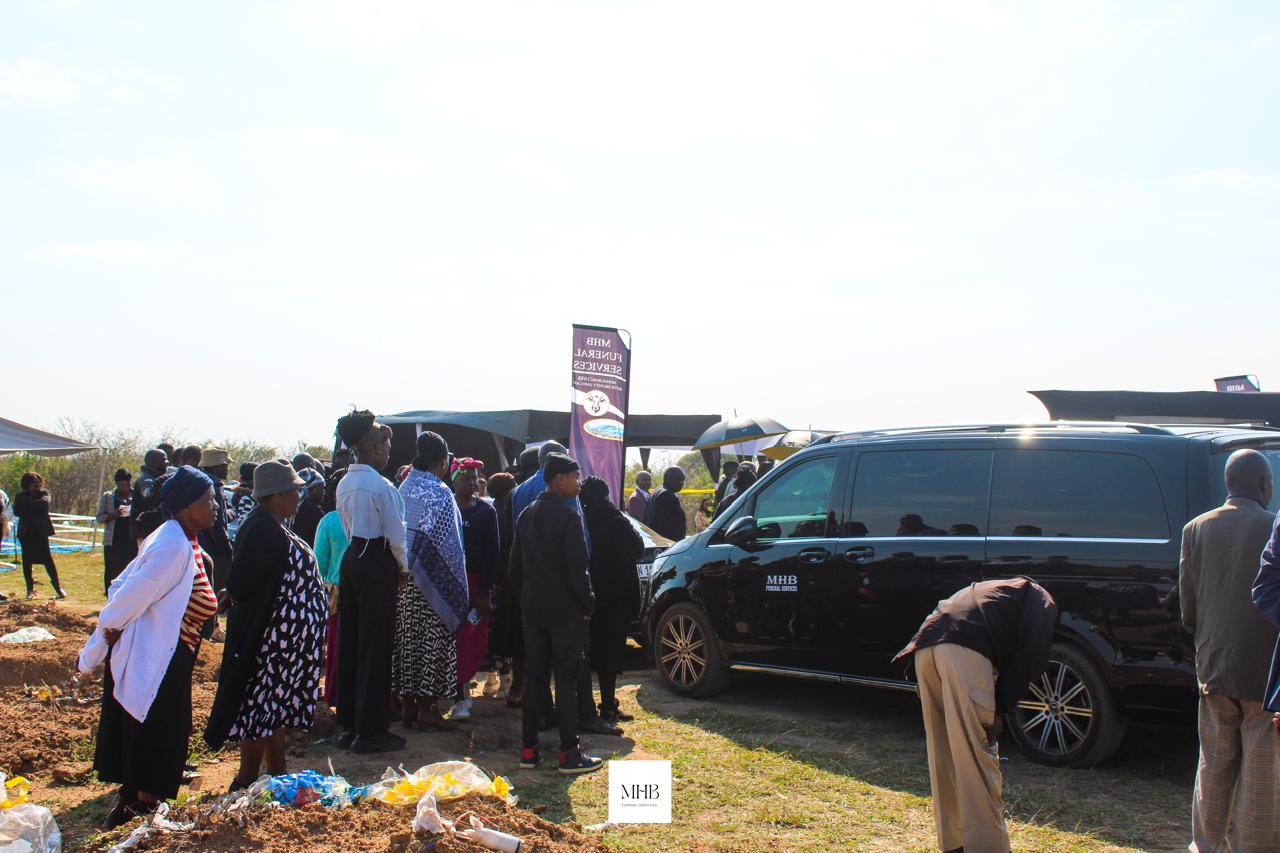 MHB branded banner and family vehicle at a graveside service in Hammanskraal
