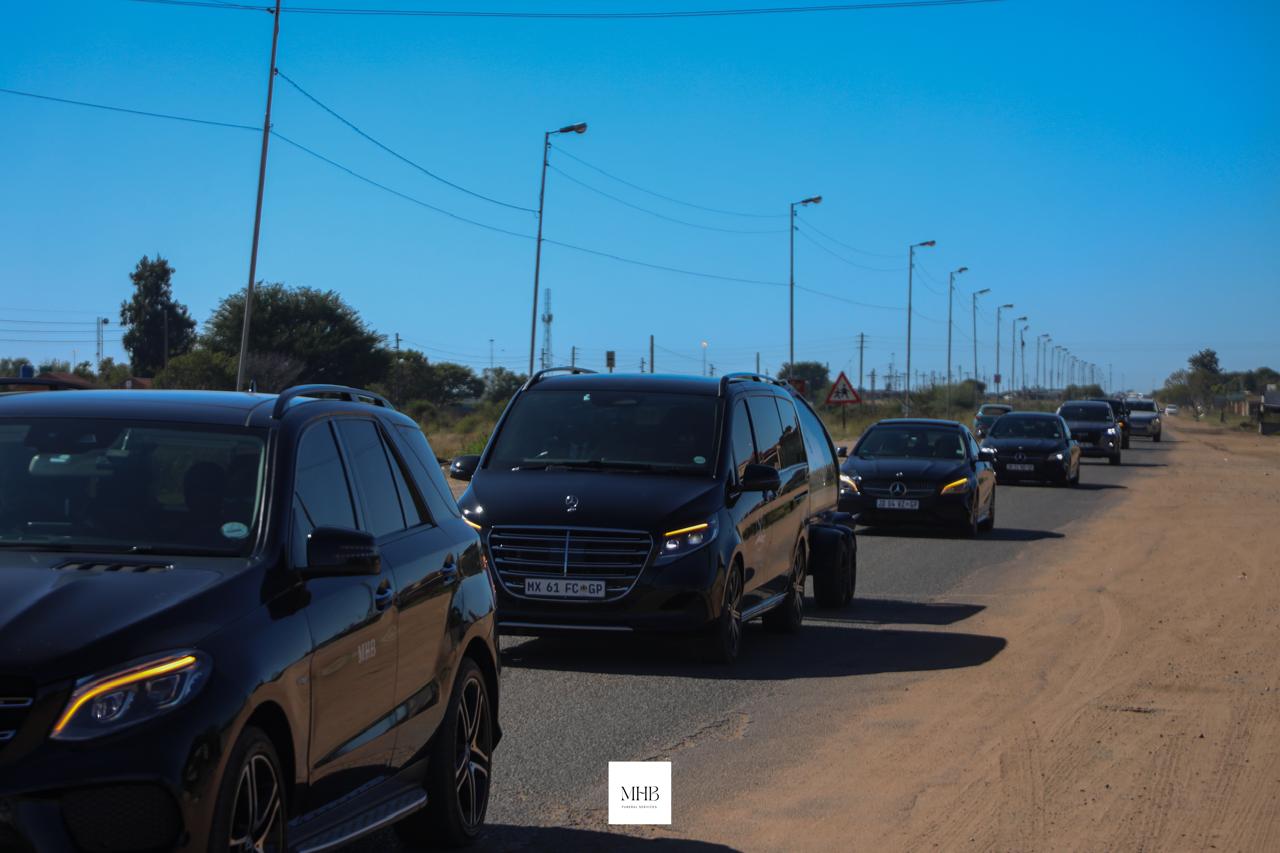 Long MHB funeral procession travelling along a road