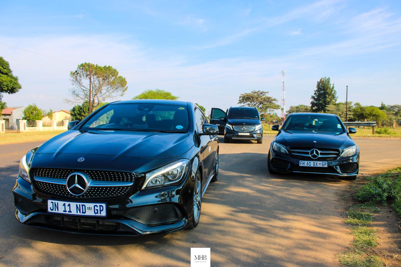 Three black MHB Mercedes-Benz family cars parked before a funeral service